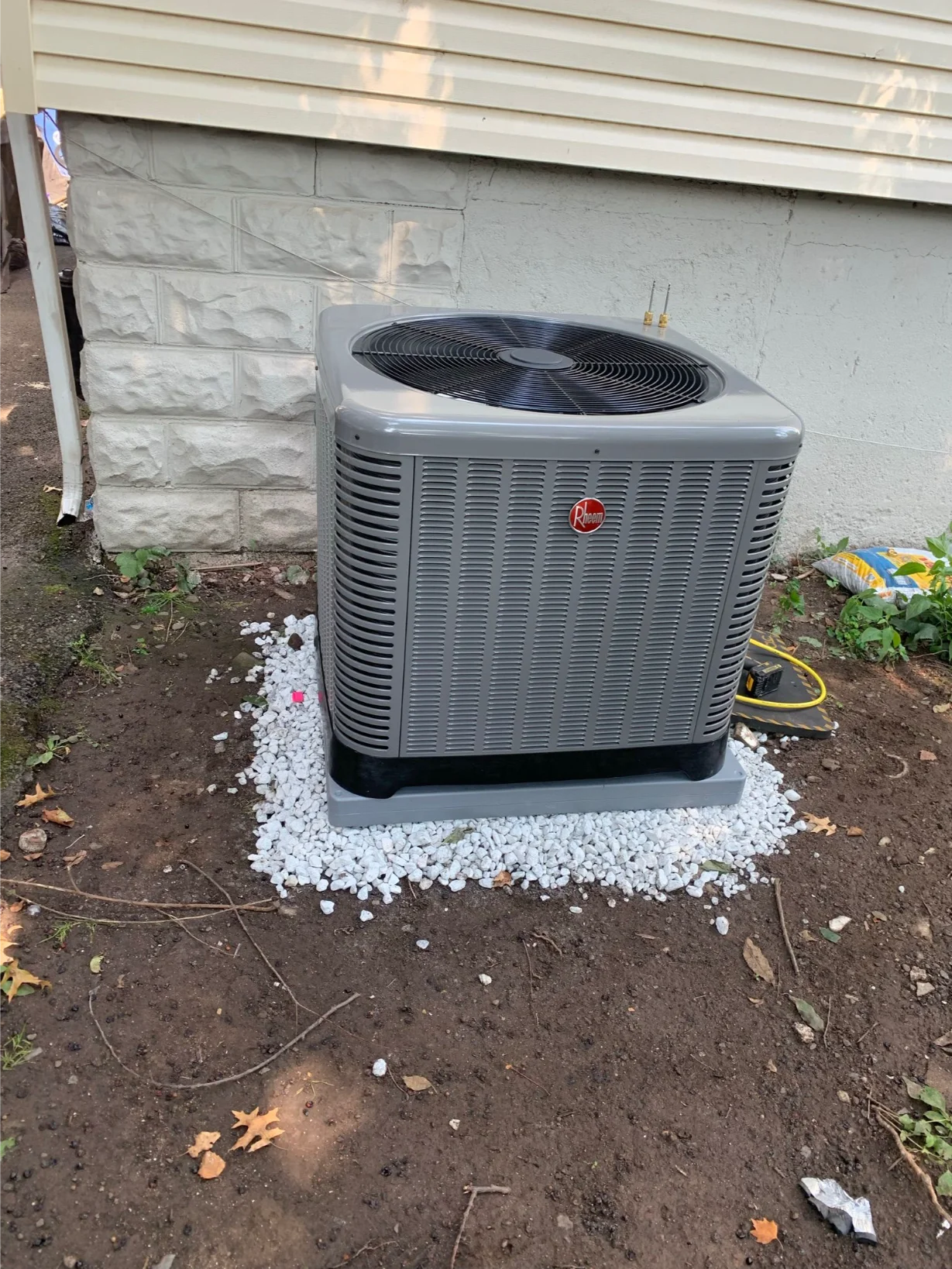 Rheem outdoor AC unit newly installed next to a house with a stone foundation